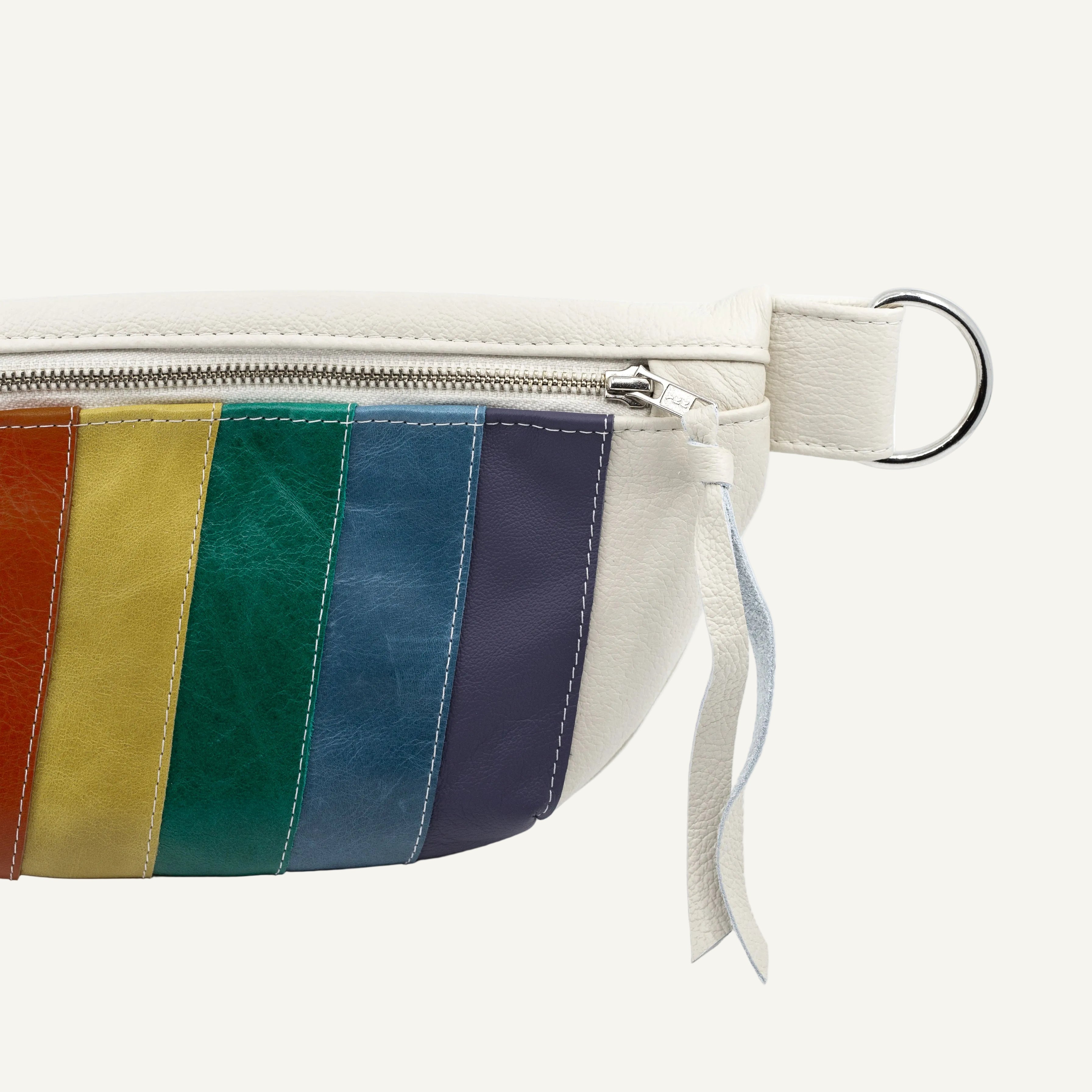A close-up of a cream-colored leather pouch with a rainbow stripe design on the front pocket, featuring a silver zipper, metal ring, on a white background.