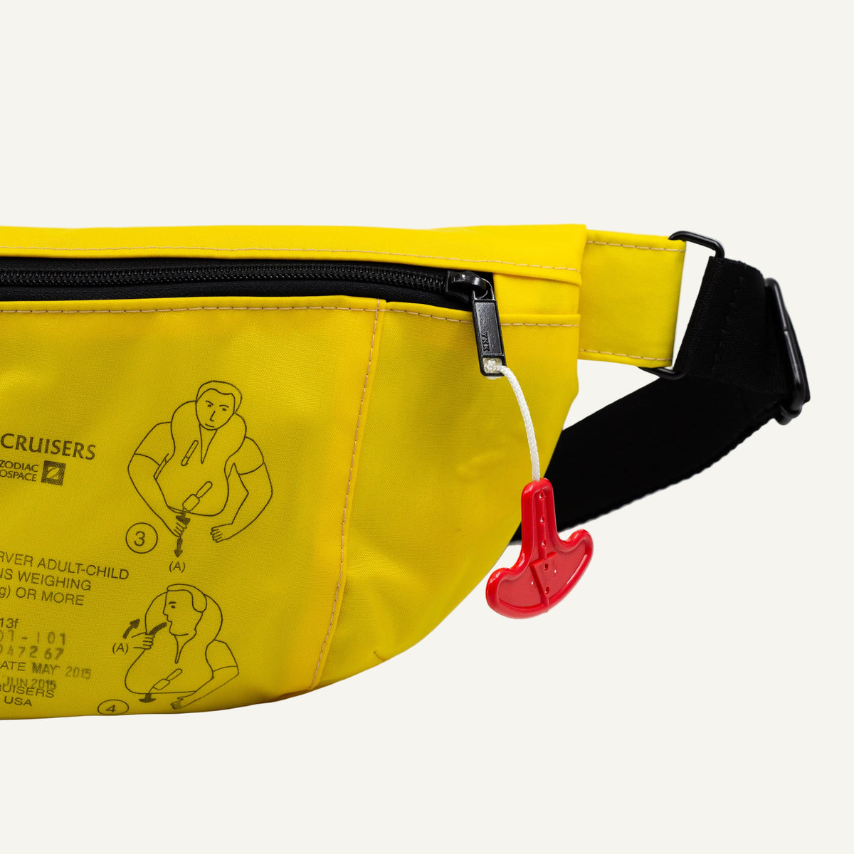 A bright yellow fanny pack with black hardware and a black adjustable strap, featuring a printed first-aid/CPR instruction graphic and a red emergency-release toggle on the front pocket.