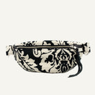 A black and off-white damask patterned waist bag with a chrome zipper and a black leather tassel pull, shown against a plain white background.