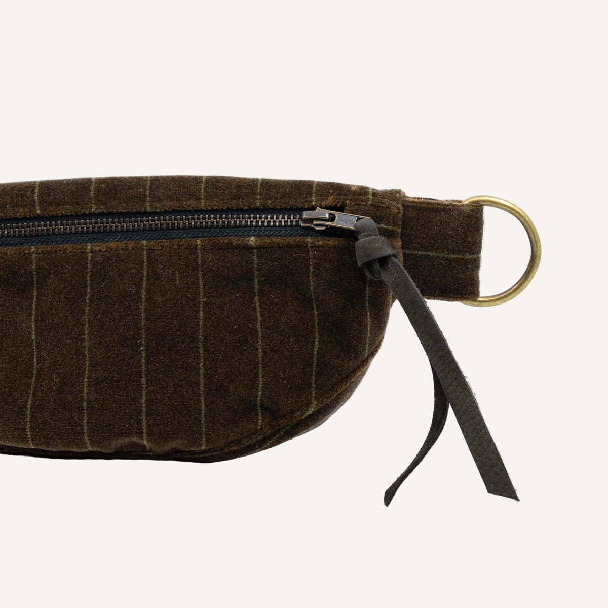 A close-up of a dark brown pinstriped fabric belt bag with a black zipper, black leather strap, and a brass ring on a white background.