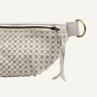 Close-up of a woven clutch or pouch in off-white and beige tones, featuring a zipper closure, a leather strap, and a gold-tone ring detail on a white background.
