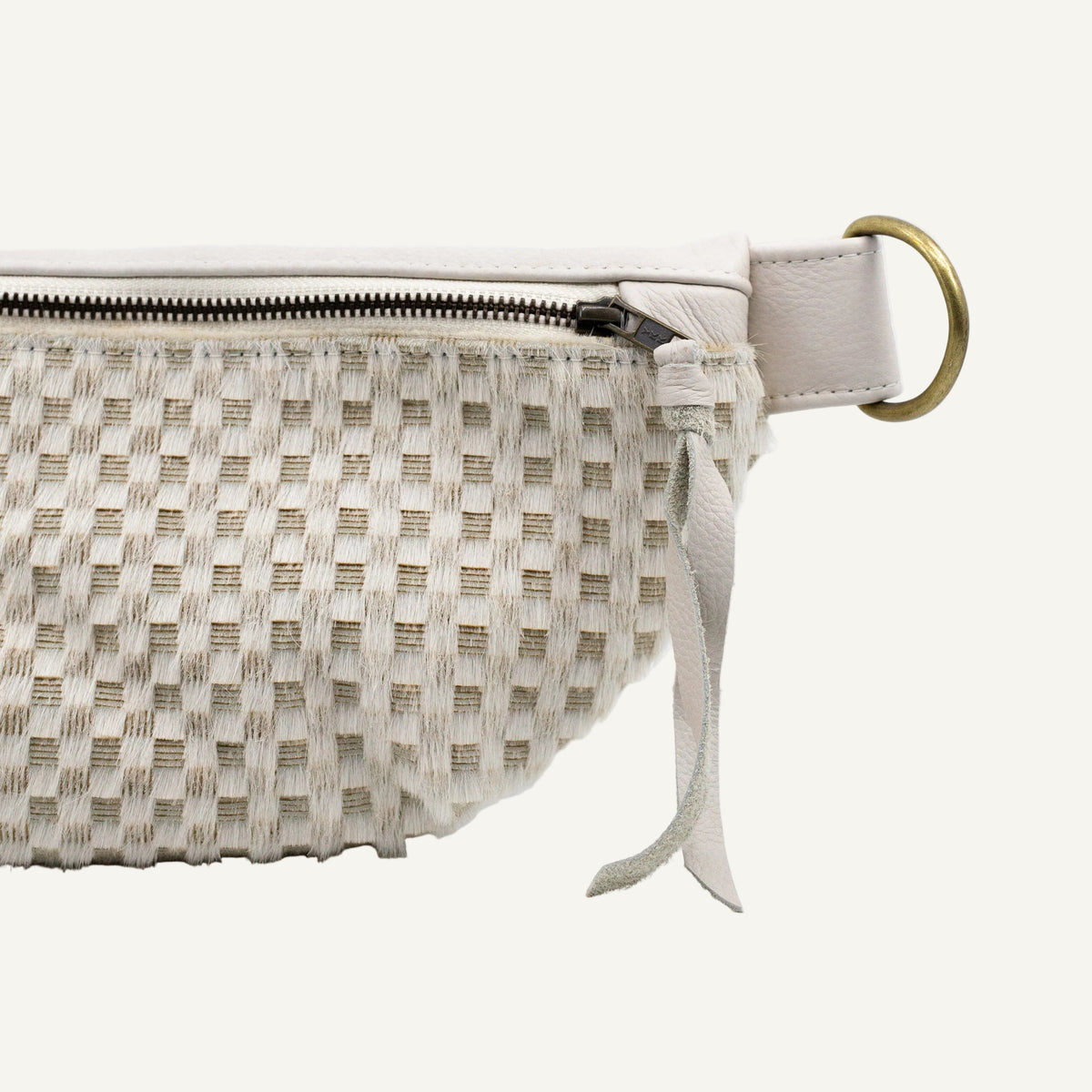 Close-up of a woven clutch or pouch in off-white and beige tones, featuring a zipper closure, a leather strap, and a gold-tone ring detail on a white background.