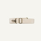 A light beige leather belt with antique bronze hardware, including a buckle, a lobster clasp, and a D-ring, laid flat on a light gray background.