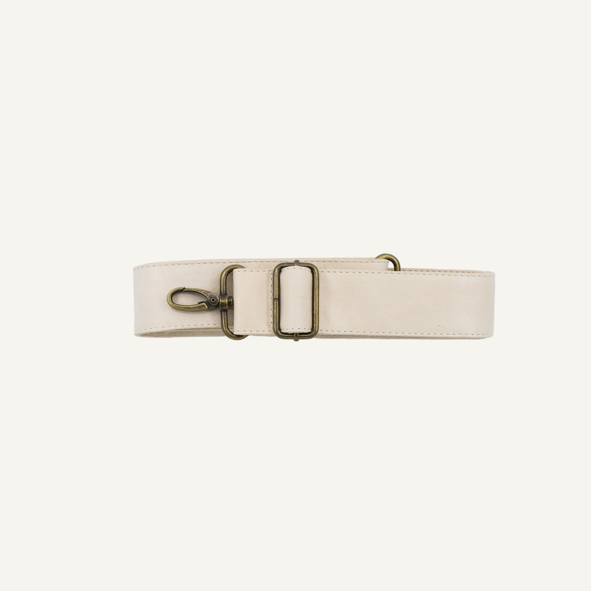 A light beige leather belt with antique bronze hardware, including a buckle, a lobster clasp, and a D-ring, laid flat on a light gray background.