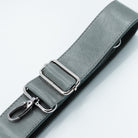 A close-up of a gray leather strap with silver metal hardware, including a rectangular buckle and a lobster clasp, on a clean white background.