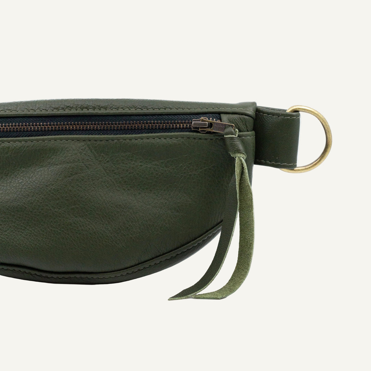 Close-up of an olive green faux-leather belt bag with a top zipper, a hanging green fabric pull, and a brass-tone metal ring on a white background.