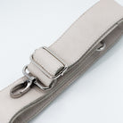 A close-up of a light beige pebbled leather strap with silver-tone metal hardware, including a buckle, adjustment loop, and lobster clasp, on a clean white background.