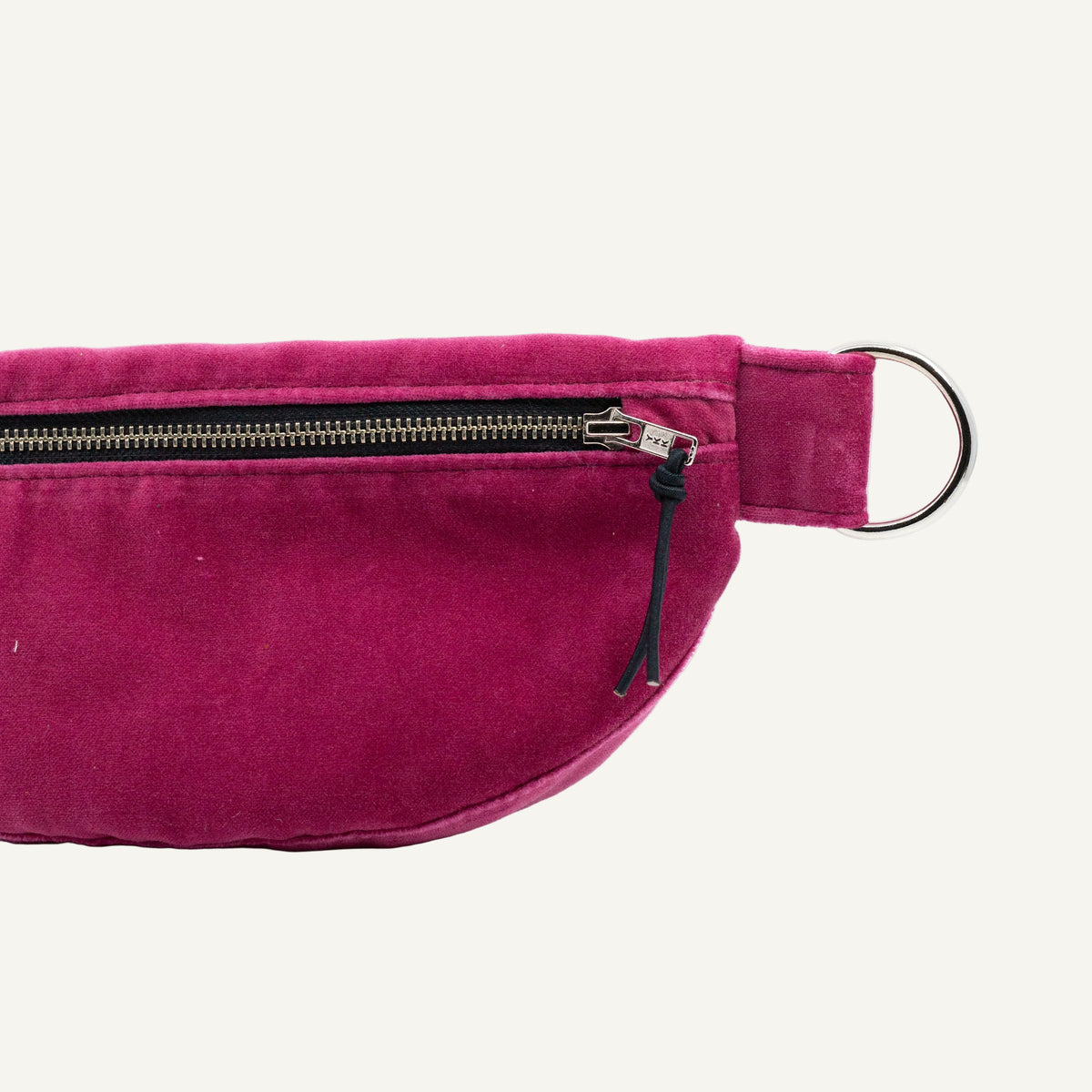 A close-up of a magenta pink velvet pouch with a black zipper, silver metal hardware, and a black drawstring tassel, set against a plain white background.