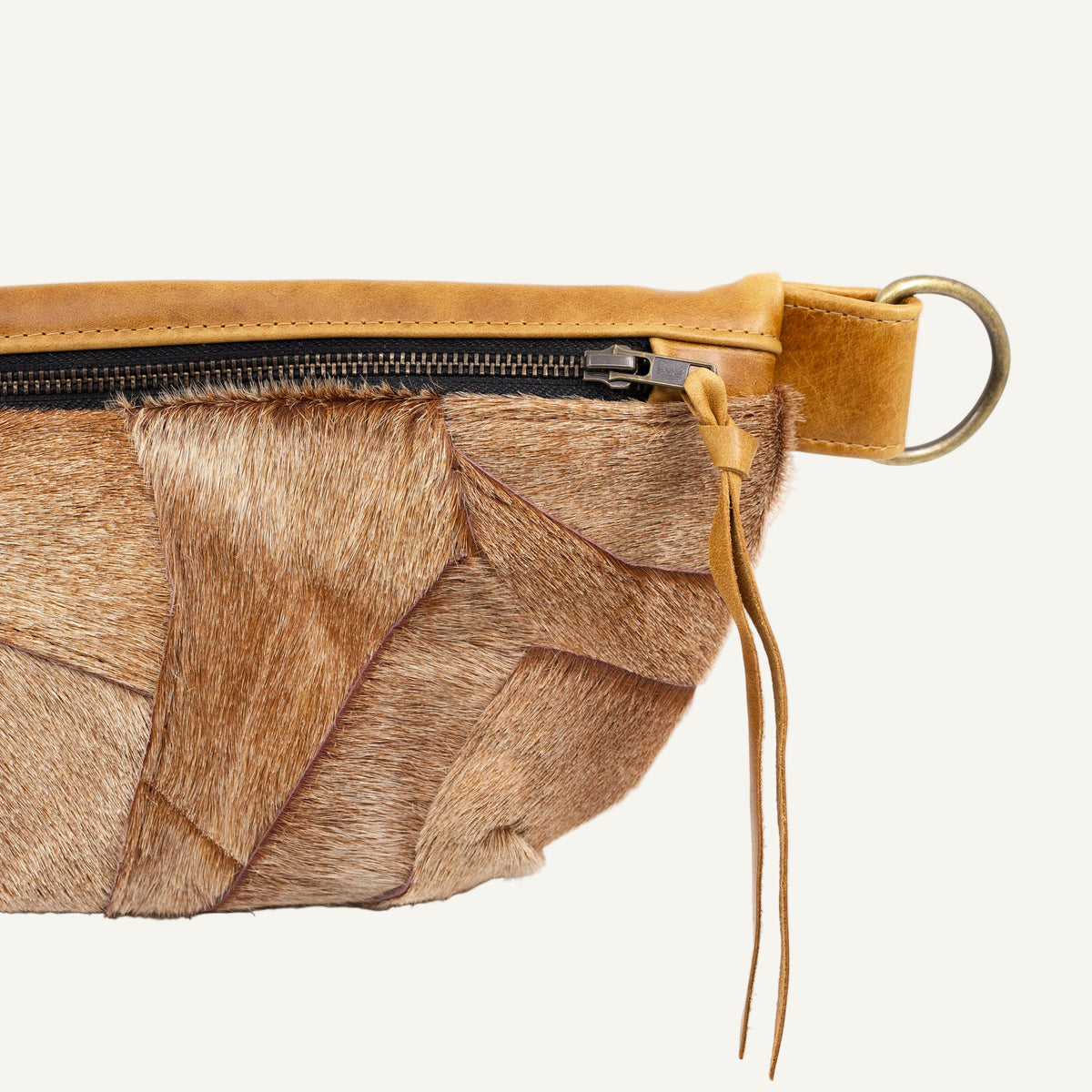 Close-up of a brown and beige animal-print fur or hair wrap bag with a tan leather zipper trim and a brass ring on a white background.