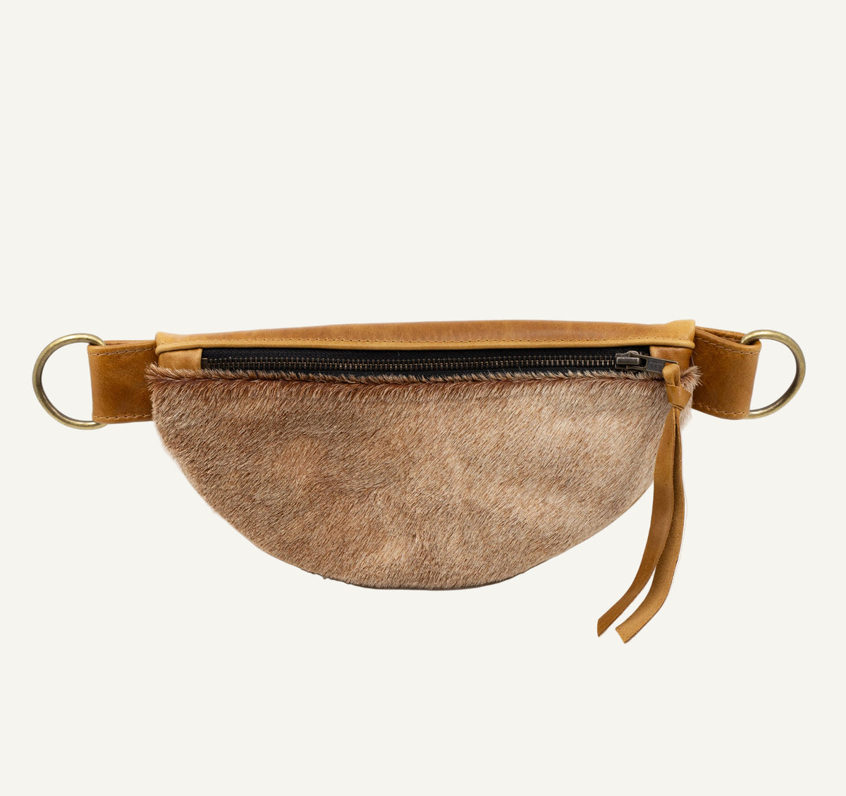A crescent-shaped belt bag featuring a brown and beige animal fur body, tan leather trim, a black zipper, and brass hardware rings on a white background.